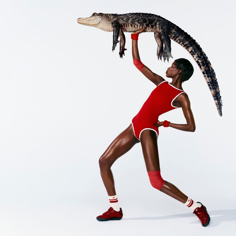 A woman in front of a white background wearing Gator Run shoes while holding an alligator. 